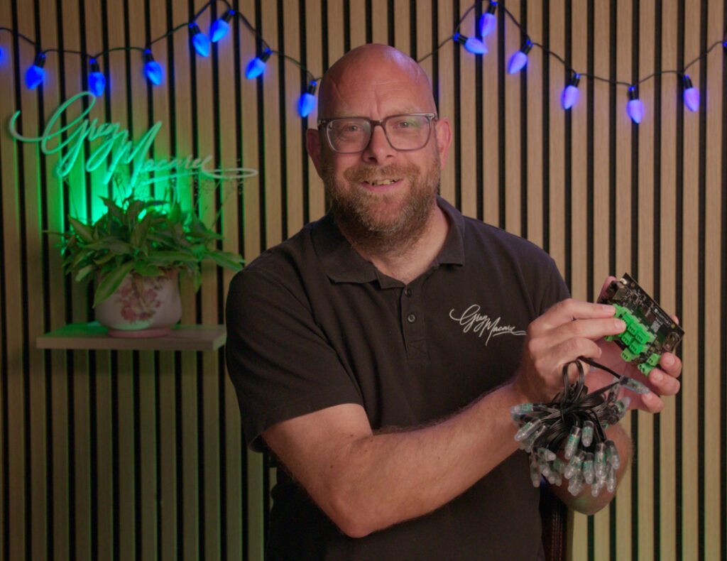 Greg smiling and holding an LED pixel controller and string lights in his lighting studio